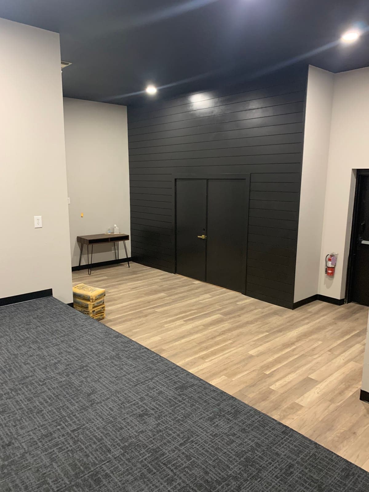 Commercial interior finished by Anaya's Touch Renovations: a black shiplap accent wall with double doors, recessed lighting, and wood-look vinyl plank meeting carpet tile.